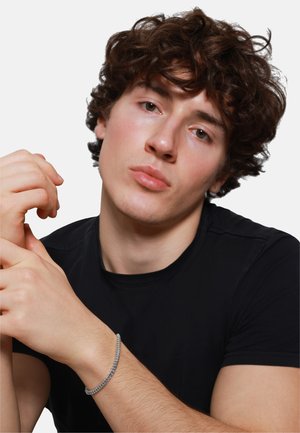 Silver chain bracelet on wrist; features interlocking links and a polished finish. Model wearing black shirt, facing forward.