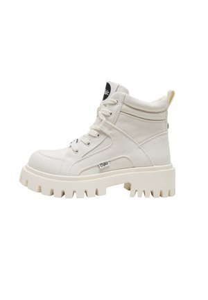 Botte montante en toile couleur blanc cassé avec semelle crantée épaisse, col rembourré, avant à lacets et petite étiquette de marque sur le côté.