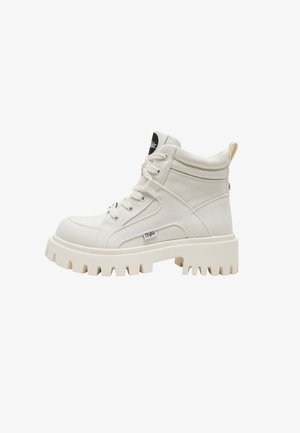 Stivaletto alto in tela color bianco sporco con suola spessa a carrarmato, collo imbottito, chiusura frontale con lacci e piccolo tag con marchio sul lato.