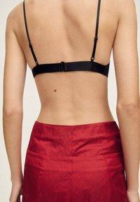 Black bra with thin straps and a clasp closure, paired with a red skirt featuring a smooth texture and back pockets.
