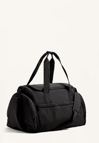 Zwarte duffelbag gemaakt van gladde stof, voorzien van dubbele handvatten aan de bovenkant, een afneembare schouderriem en een voorvak met ritssluiting.