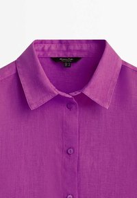 Chemise en lin violet avec un col classique, un design à boutons sur le devant et une texture lisse. Comprend cinq boutons et une étiquette de marque à l'intérieur du col.