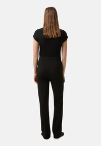 Schwarzes, figurbetontes Oberteil mit kurzen Ärmeln, kombiniert mit schwarzen, maßgeschneiderten Hosen. Glatte Textur und klare Linien. Rückansicht zeigt ein minimalistisches Design.