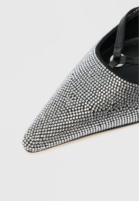Black pointed-toe shoe covered in small silver rhinestones. Features a black strap with a circular metal accent. Smooth texture.