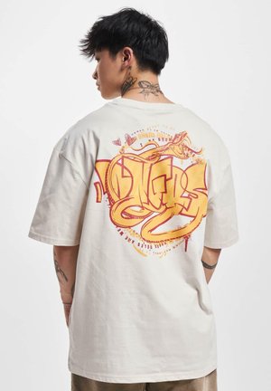Cremefarbener Baumwoll-T-Shirt mit kurzen Ärmeln. Großes grafisches Druckmotiv auf der Rückseite mit gelbem und rotem abstraktem Design, einschließlich Text und Schlangenmotiven.