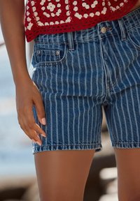 Shorts en denim avec des rayures verticales bleues et blanches, dotés d'une taille haute, de poches avant et d'un ourlet brut. La texture est légèrement texturée.