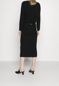 Svart stickad tröja och midi kjol-set. Tröjan har långa ärmar och en rundad halsringning. Kjolen har en åtsittande design och en bakre slits. Svarta mules.