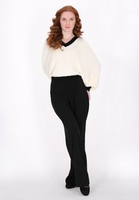 Maglione overdimensionato in crema con scollatura a V nera e polsini neri, abbinato a pantaloni neri a vita alta e larghi, e scarpe nere senza lacci.