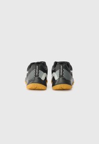 Schwarze Sportschuhe mit strukturierter schwarzer Oberfläche, silbernen Akzenten und einer ausgeprägten gelben Gummisohle mit Zickzackmuster.