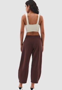 Bruine wijde broek en een beige geribbelde crop top. Het achteraanzicht laat de brede bandjes van de top zien en de casual pasvorm en gladde textuur van de broek.