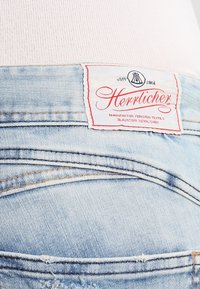 Světlemodré džíny z denimu s distressed texturou, na zadním pásku mají červený a bílý štítek s nápisem "Herrlicher".