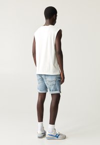 White sleeveless cotton shirt, light blue denim shorts, rolled cuffs, gray and blue sneakers, worn with white crew socks, viewed from the back.