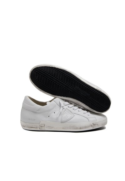 Baskets en cuir blanc avec une texture lisse, bout arrondi, lacets plats et semelle extérieure en caoutchouc noir présentant un motif en chevrons. Détail de marque subtil.