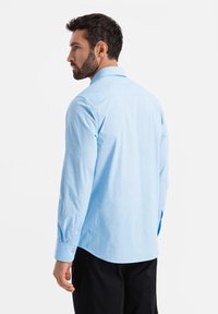 Camicia a maniche lunghe di cotone azzurro chiaro, con colletto classico, polsini abbottonati e orlo curvo.