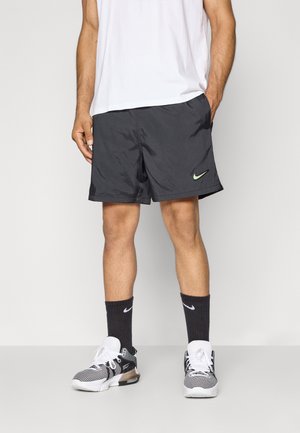 Sorte Nike shorts med et grønt logo, parret med sorte Nike sokker og hvide sneakers. Shortsene har en let, glat tekstur.