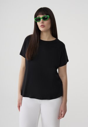 T-shirt nera a maniche corte in un tessuto morbido con scollo rotondo, abbinata a pantaloni bianchi. Modello con occhiali da sole verde brillante.