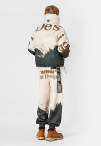 Chaqueta acolchada con estampado de montaña en tonos pastel y texto marrón, combinada con pantalones a juego y botas color canela con suela gruesa.