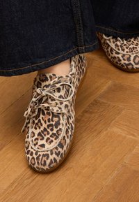 Leopardenmuster Flachschuhe aus weichem Material, mit runder Zehenpartie, Schnürdesign und hellfarbener Gummisohle. Hintergrund mit Holzfußboden.