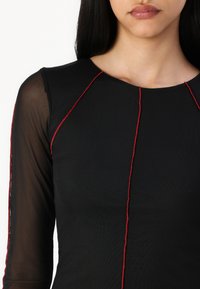 Must have pikkade siidiste varrukatega must topp, ümmarguse kaeluse ja kontrastse punase õmblusega, mis toob esile visuaalse aktsendi.