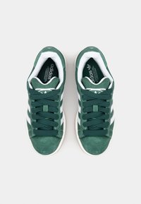 Gröna mockasneakers har vita tre-stripes accenter, rund tå och platta skosnören. Mjuk innersula och texturerad yttersula fulländar designen.