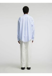 Modra in bela srajca z dolgimi rokavi s črtami, sproščen kroj, kombinirana s sproščenimi belimi hlačami in črnim obutvom. Tkanina iz teksturiranega bombaža.