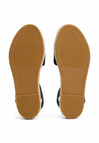 Sandalias negras con suela de goma texturizada, que presentan un acento de esparto beige a lo largo del borde y detalles de marca en el talón.