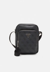 Černá crossbody taška Guess s monogramovým vzorem, přední kapsou na zip, stříbrným trojúhelníkovým logem a nastavitelným ramenním popruhem na bílém pozadí.