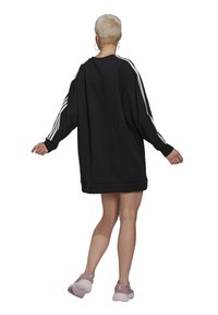 Abito felpa nero oversize con strisce laterali bianche e maniche lunghe, con orlo a costine; modello che indossa sneakers rosa.