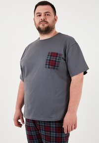 Szara bawełniana koszulka z okrągłym dekoltem i krótkimi rękawami, z kieszonką w czerwono-niebieską kratkę po lewej stronie.