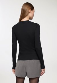 Czarny, dopasowany sweter z długim rękawem i okrągłym dekoltem, o gładkiej fakturze i prążkowanych detalach na mankietach, zestawiony z szarymi szortami.