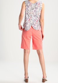 Haut sans manches fleuri avec un ourlet arrondi dans des couleurs pastel ; shorts corail ; sandales à talons blanches ; tissu lisse ; coupe décontractée.