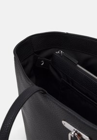 Černá kožená taška přes rameno s texturovaným povrchem, obsahující kapsu na zip a hladký vnitřní podšívku. Zahrnuje jeden popruh na rameno.