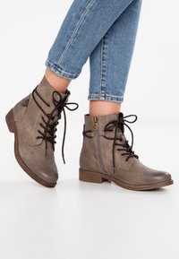 Botas de tobillo marrones con un acabado texturizado, cordones y una cremallera en el costado. Tacón bajo y punta redondeada para un estilo casual.