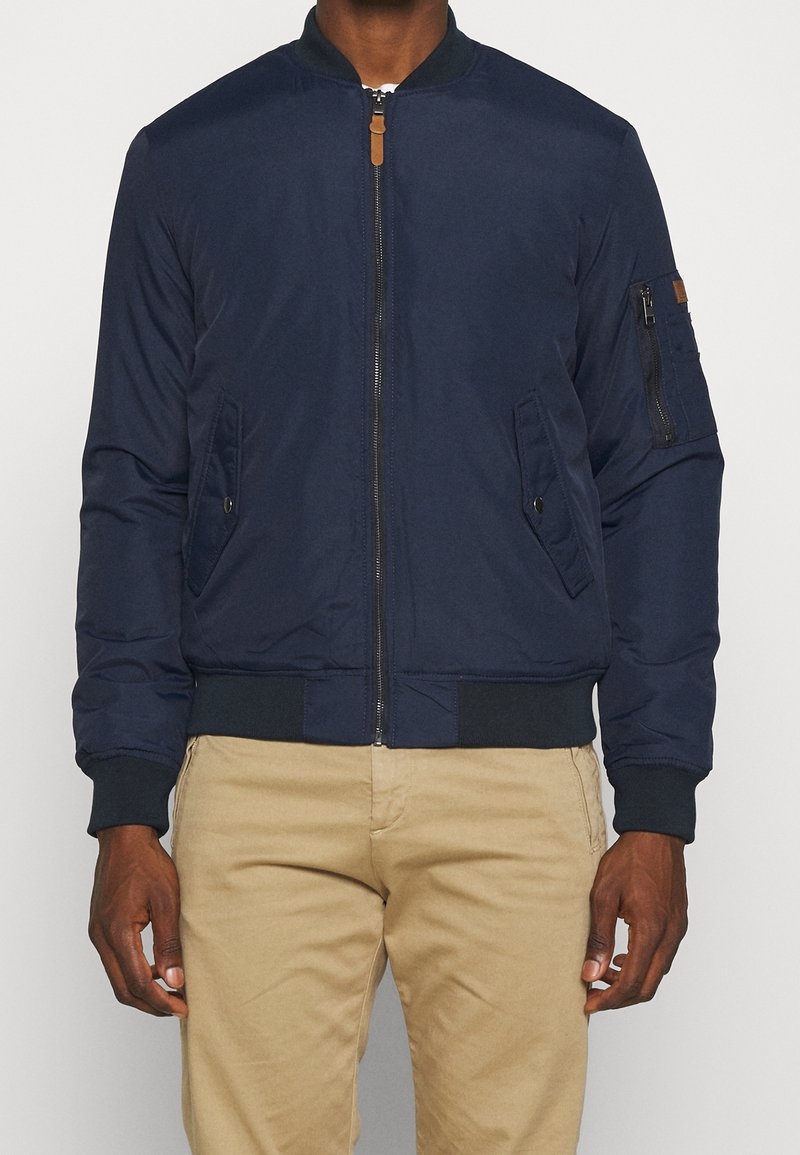 Giubbotto bomber blu navy con zip, polsini a coste, tasche laterali e tasca sul braccio con dettaglio in pelle. Tessuto dalla consistenza liscia.