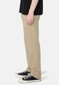 Beige chinos with a straight-leg cut and side pockets, paired with black canvas sneakers featuring white accents and laces.