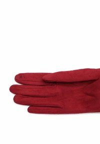 Un paio di guanti in suede rosso distesi, che mostrano i dettagli cuciti sulle dita e un piccolo emblema decorativo nell'area del polso.