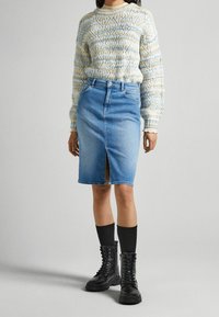 Gonna a tubino in denim azzurro chiaro con uno spacco frontale, abbinata a un maglione lavorato a maglia con fantasia e stivali militari neri, completata da calze alte fino al ginocchio.