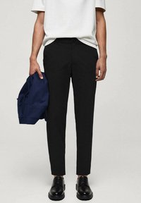 Črne krojene hlače z ožjim krojem, opremljene z zankami za pas in gumbom za zapiranje. Nosi se z belo majico in mornarsko modrim jarkom.