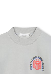 Sweatshirt gris clair avec col côtelé. Présente un graphique coloré avec le texte "METTEZ VOS MAINS EN L'AIR !" et un design de grenouille à l'avant.