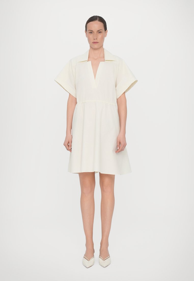 Robe blanche avec un décolleté en V, des manches courtes et larges, et une taille ajustée. Tissu lisse, jupe évasée et design minimaliste.