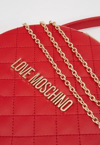 Červená prošívaná kabelka z umělé kůže s pozlaceným řetízkem a vyraženým logem "LOVE MOSCHINO" v metalickém provedení.