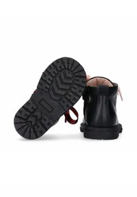 Stivali alla caviglia in pelle nera con suola in gomma texture, caratterizzati da un accento in nastro rosso e un design con punta arrotondata.