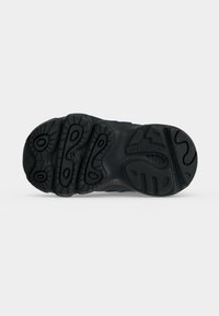 Μαύρη λαστιχένια σόλα παπουτσιού New Balance που δείχνει υφασμένους σχεδιασμούς πέλματος και το χαραγμένο όνομα της μάρκας κοντά στον αψίδα.