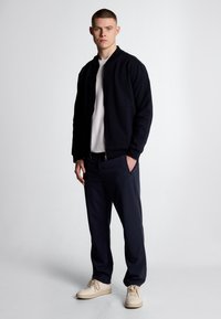 Giacca bomber blu navy, t-shirt bianca, pantaloni blu navy e sneakers crema. Tessuto morbido, chiusura con zip, polsini e orlo a coste. Vestibilità casual, design minimalista.