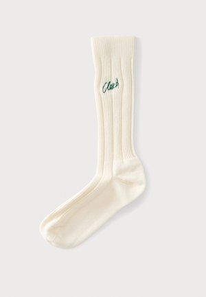 Chaussette côtelée de couleur crème unique avec le mot brodé en vert "Closed" près du haut du bord-côte, présentée à plat sur un fond clair.