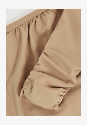 Beige Kleidungsstück mit einem gerafften Manschettendetail, aus glattem Stoff gefertigt. Die Textur wirkt weich mit dezenten Nähten entlang der Kanten.