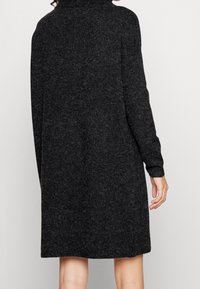 Texturerad svart klänning i sweaterstil med hög krage, långa ärmar och avslappnad passform, som sträcker sig till mitten av låret.