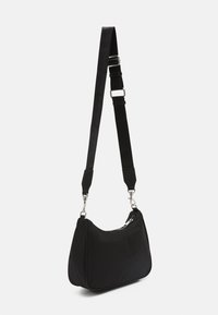 Sac à bandoulière noir avec sangle ajustable, fermeture éclair argentée et attaches métalliques sur fond blanc.