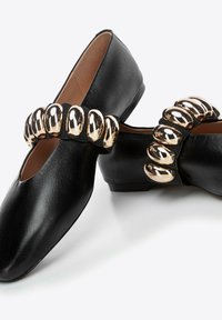 Ballerine in pelle nera con tacco basso, caratterizzate da una distintiva fascia di accenti dorati lucidi e un design con ritagli sulla parte superiore.