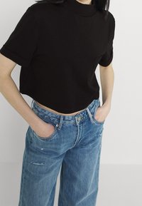 Svart kortärmad T-shirt med hög hals, kombinerad med ljusblå högmidjade jeans med slitna detaljer.